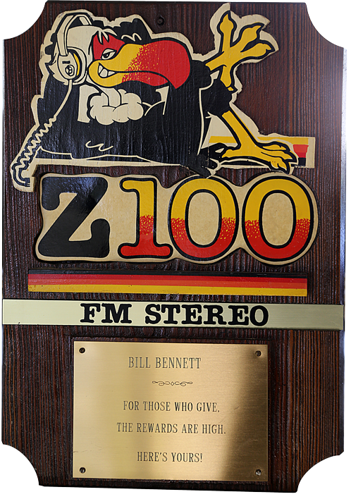 wooden plaque with a cutout of the Z100 buzzard and the Z100 logo. Inscription reads &lquo;For those who give the rewards are high. Here's yours&rquo;